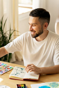 Artist man smiling, drawing watercolor. sitting,holding paintbrush.looking for inspiration.lifestyle