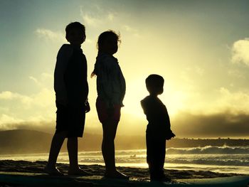 Silhouette men standing on beach against sky during sunset
