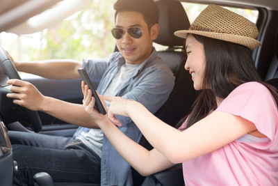 Close-up of girlfriend pointing on mobile phone with boyfriend driving car