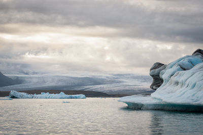 Icebergs in sea against cloudy sky