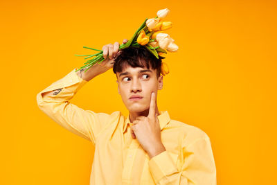 Portrait of young woman standing against yellow background