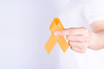 Close-up of hand holding yellow leaf against white background