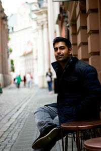 Portrait of young india  man sitting on seat at cafe in european city of poland, low angle of man 