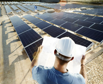 Back view of engineer looking at plan in front of solar plant