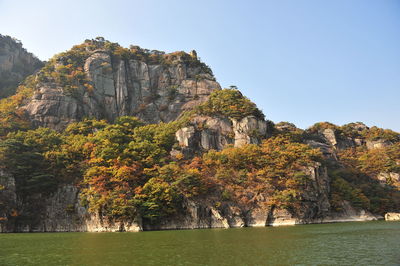 Scenic view of cliff by trees against clear sky