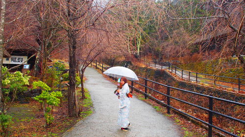 Rear view of woman standing on umbrella during rainy season