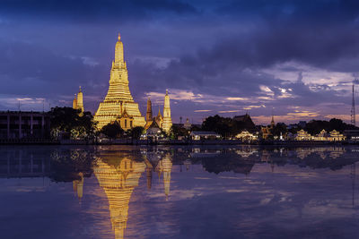 Reflection of illuminated pagoda in lake against cloudy sky