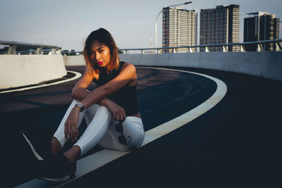 Portrait of woman sitting on road in city during sunset