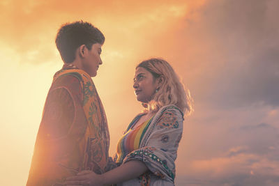 Side view of young same sex couple against sky during sunset