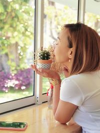 Close-up of young woman smelling cactus by window at home