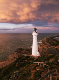 Lighthouse by sea against sky during sunset