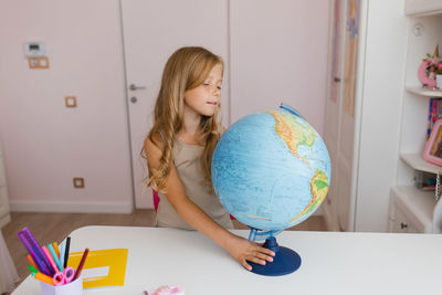 Curious child girl sitting on a chair looking with interest at the globe on the table. a cute kid 