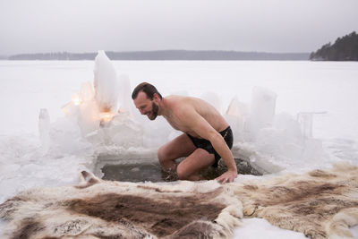 Cheerful mature man enjoying ice bath at frozen lake during vacation