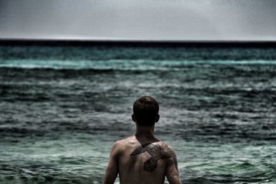 Rear view of shirtless man looking at sea