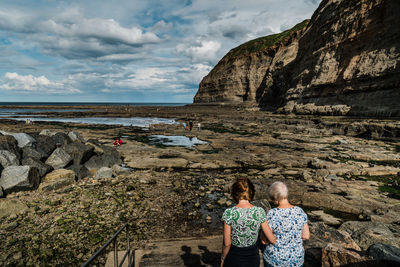 Rear view of people standing on beach against sky