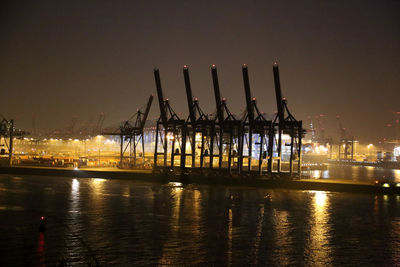 Cranes at harbor against clear sky at night