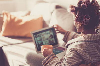 Woman holding coffee cup while video conferencing over laptop at home