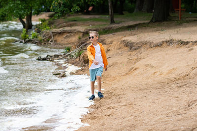 A boy in an orange shirt on the seashore. a child in sunglasses person