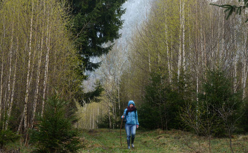 Woman walking on grassy field amidst trees at forest