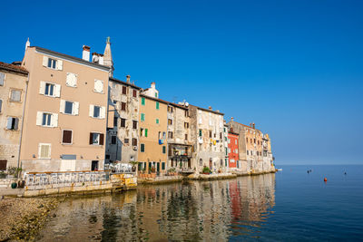 Buildings by canal against clear blue sky