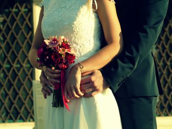 Midsection of couple with bouquet standing outdoors