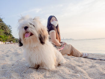 Young asian woman sitting with her fluffy puppy on the beach at pattaya. new normal lifestyle.