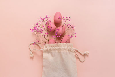 Easter composition with pink eggs and flowers arranged near bag