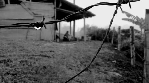 Close-up of barbed wire fence by abandoned house