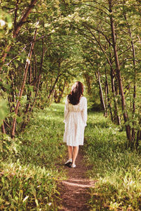 A young girl in a white dress walks in the woods