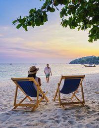 Rear view of woman sitting at beach against sky during sunset