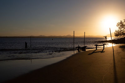 Scenic view of beach against sky during sunset with one people fishing