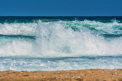 Waves splashing on shore against clear sky