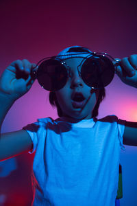 Cyberpunk boy in a white t-shirt and cap sunglasses stands against the wall and thinks