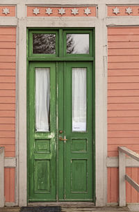 An old worn green wooden door to a pink house