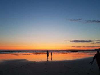 Silhouette people on beach against sky during sunset