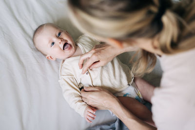 Mom changes the bodysuit of a cheerful baby after changing the diaper.