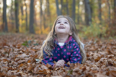 Smiling girl looking up while lying on field in forest