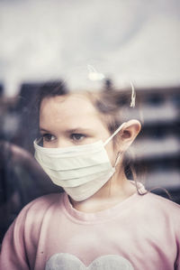 Girl wearing mask looking away seen through window