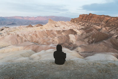 Rear view of mid adult woman sitting on rock formation against sky