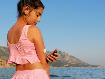  girl reads glucose level  from the white sensor on arm with cgm device before enters the sea. 