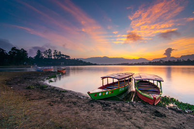 Rowboats moored in lake against sky during sunset