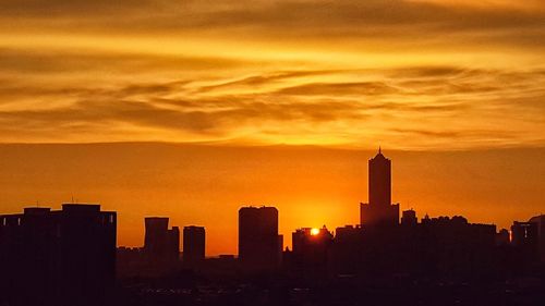 Silhouette of city against cloudy sky during sunset