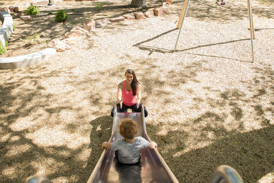 High angle view of son sliding towards mother on slide at playground