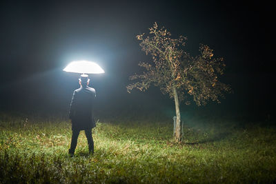 Rear view of man standing on field against sky at night