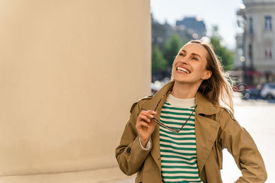 A woman laughs happily and holds glasses in her hand on the street