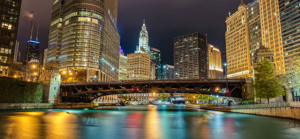 Illuminated bridge over river by buildings in city at night