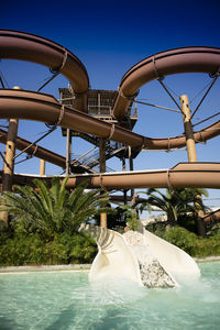 Low angle view of the slide at a water park against clear blue sky 