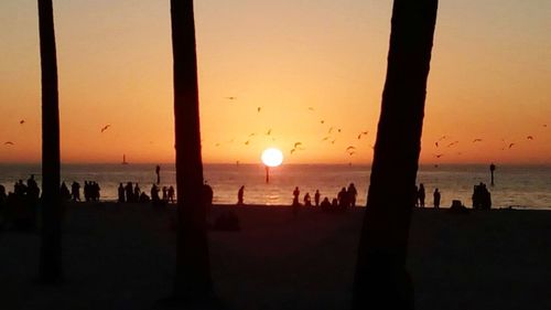 Silhouette people on beach against sky during sunset