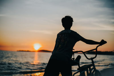 Silhouette man standing on beach against sky during sunset