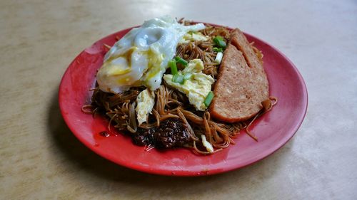 Close-up of bee hoon served with fried egg and meat in red plate